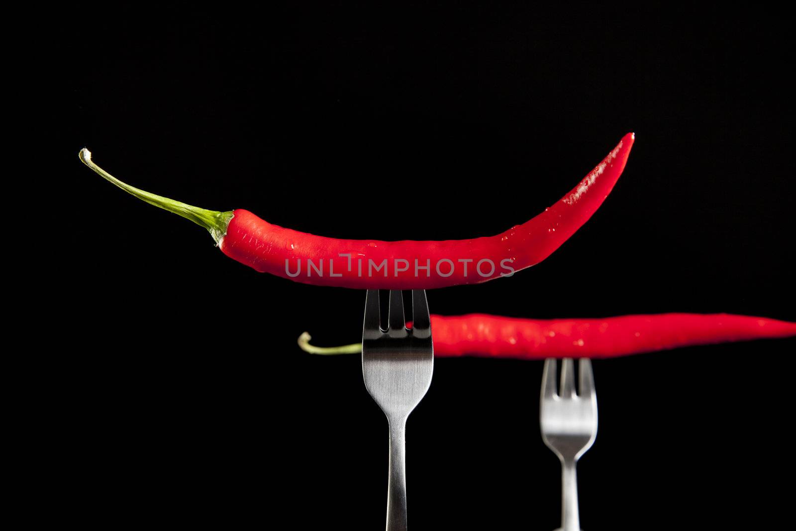 Two hot peppers on forks with black background.