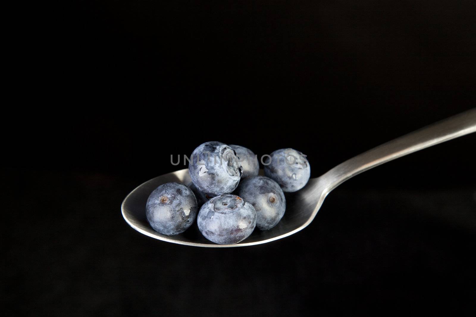 Fresh blueberries on spoon with black background.