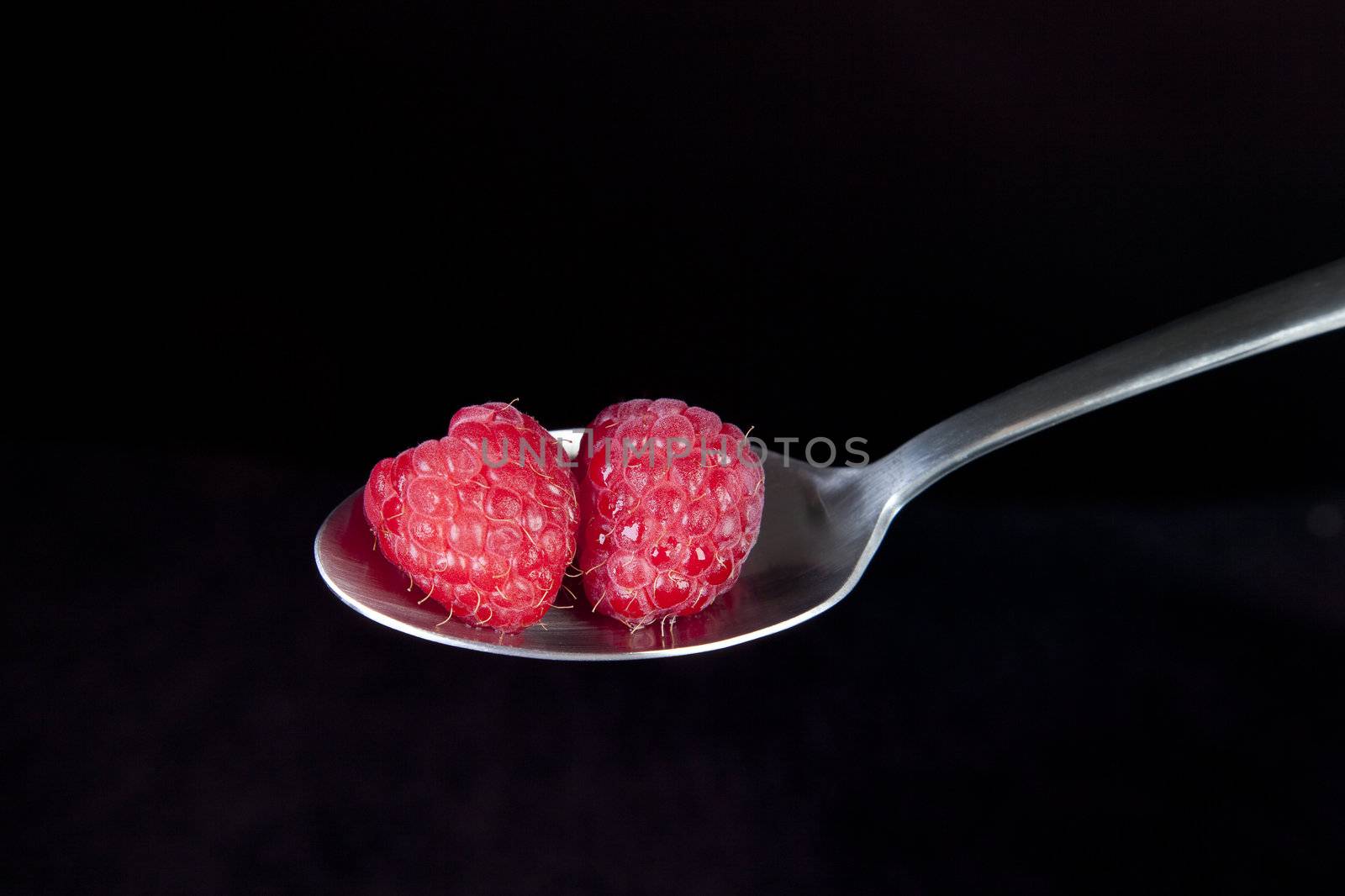 Fresh raspberries on spoon with black background.