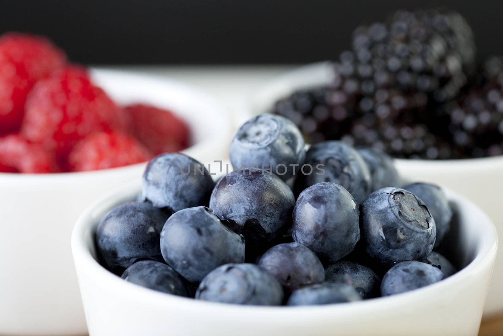 Blueberries in white bowl with raspberries and blackberries in background.
