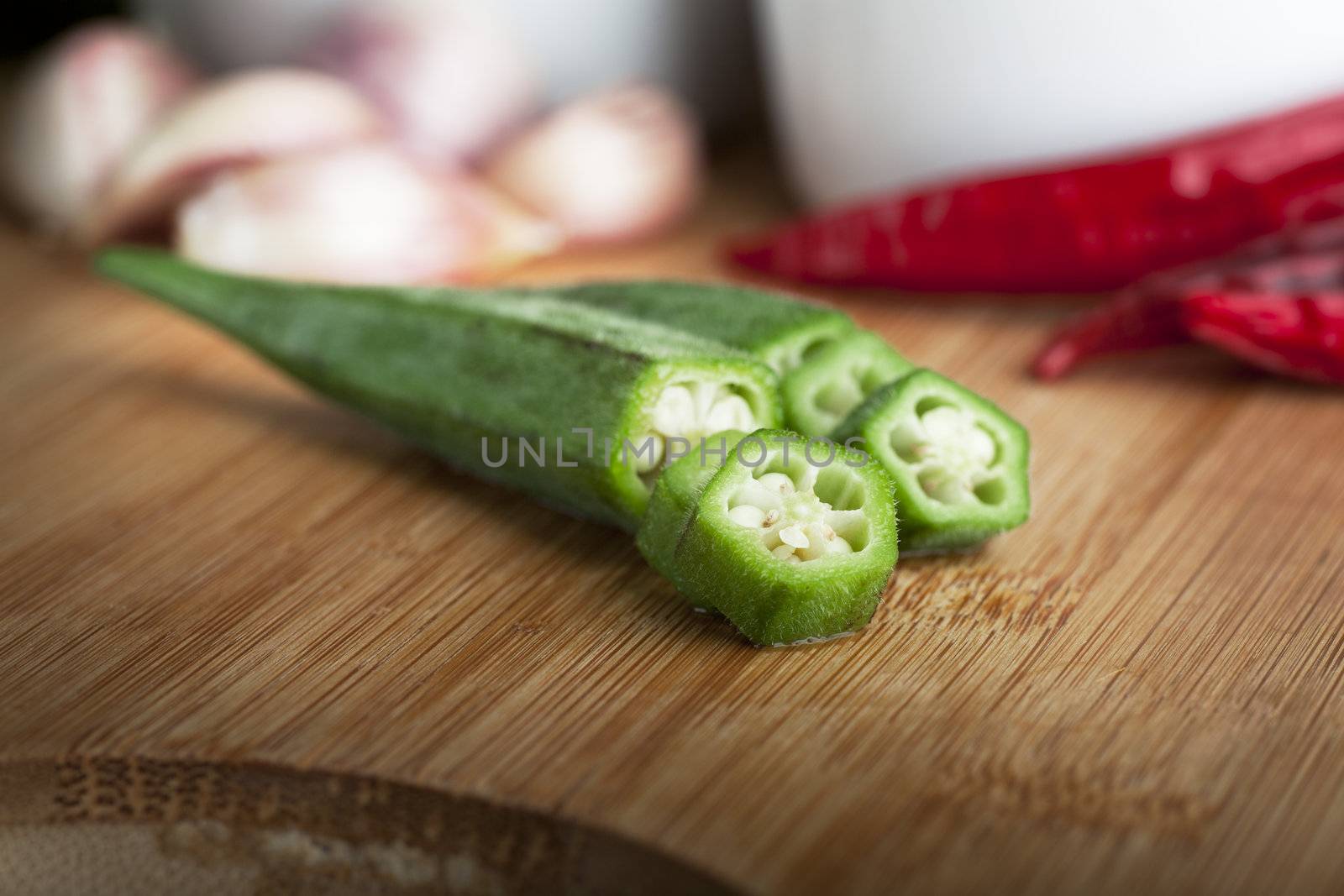 Two okra pods with slices on cutting board.