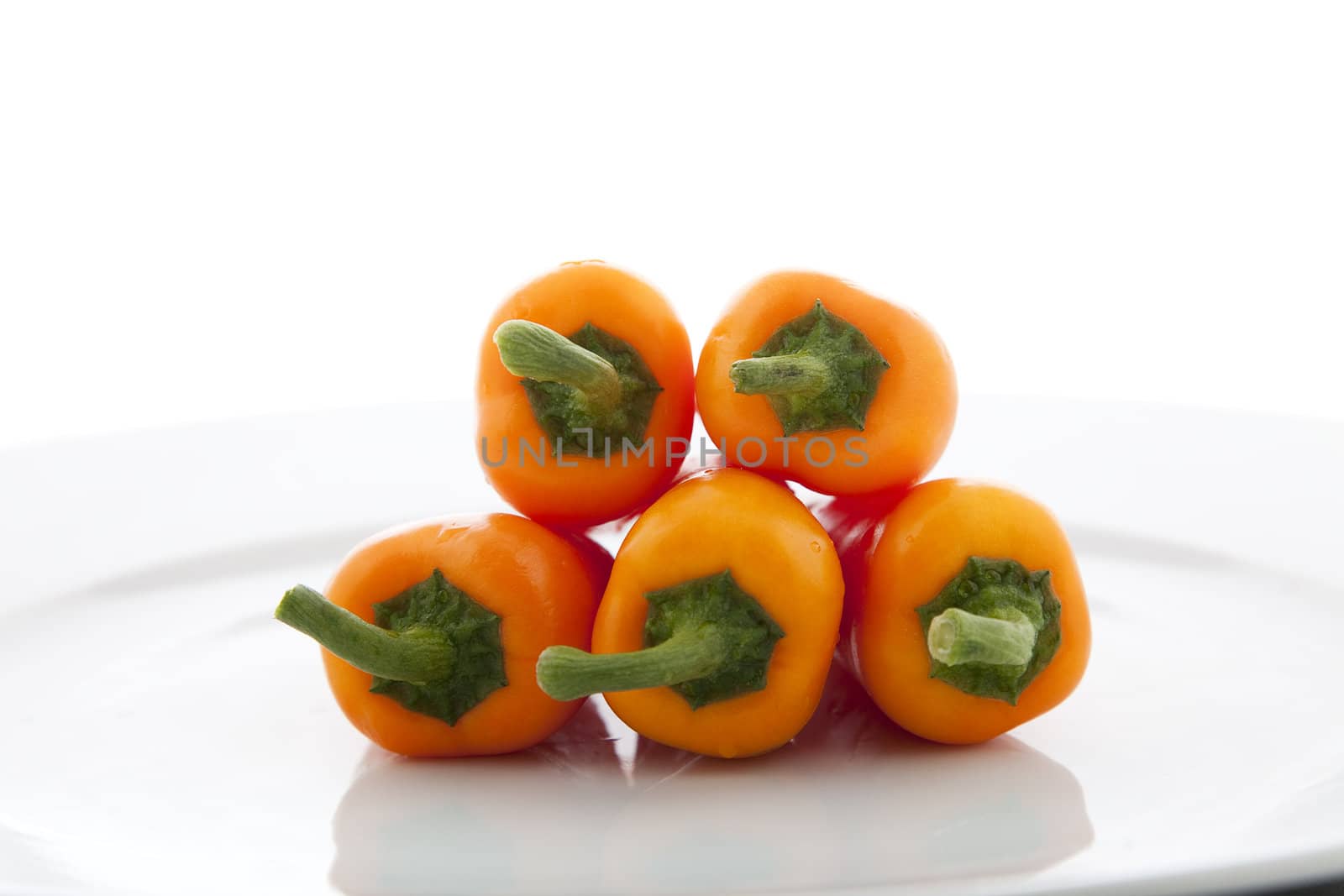 Five orange peppers on white plate.