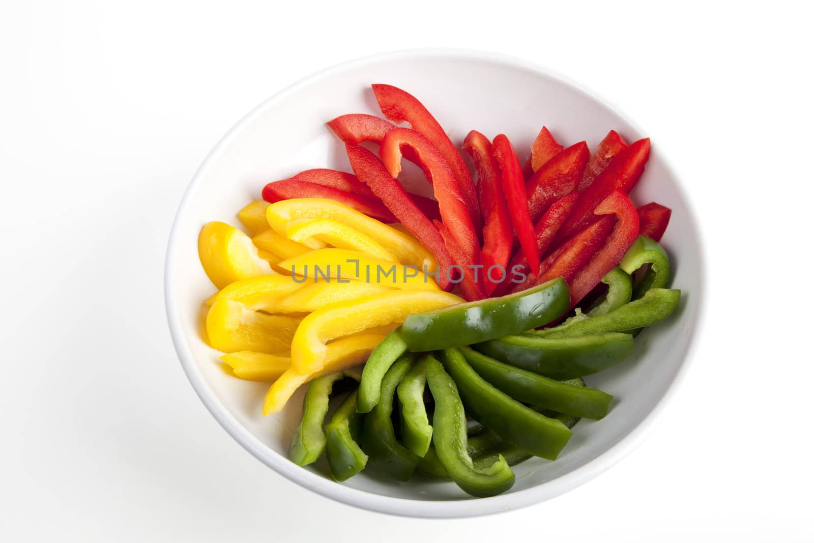 Bowl of red, yellow and green slices of bell peppers in white bowl on white background.