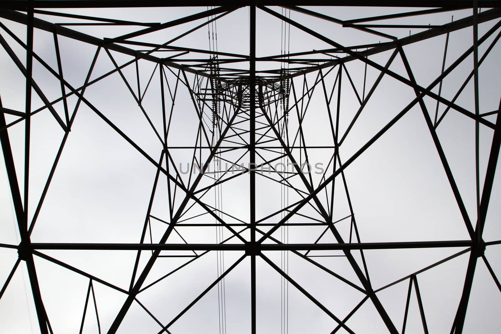 Siloette of electric power tower looking from the base to the top against cloudy sky