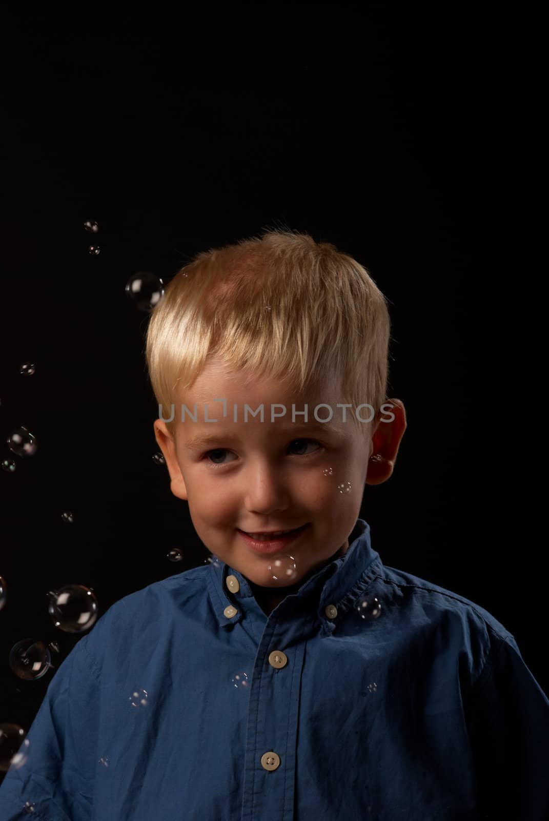 Blond boy getting soap bubbles blown in his face