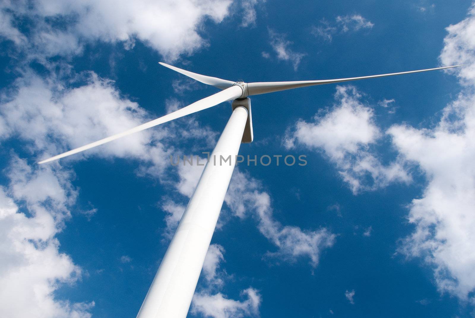 Wind mill power generator against blue cloudy sky.