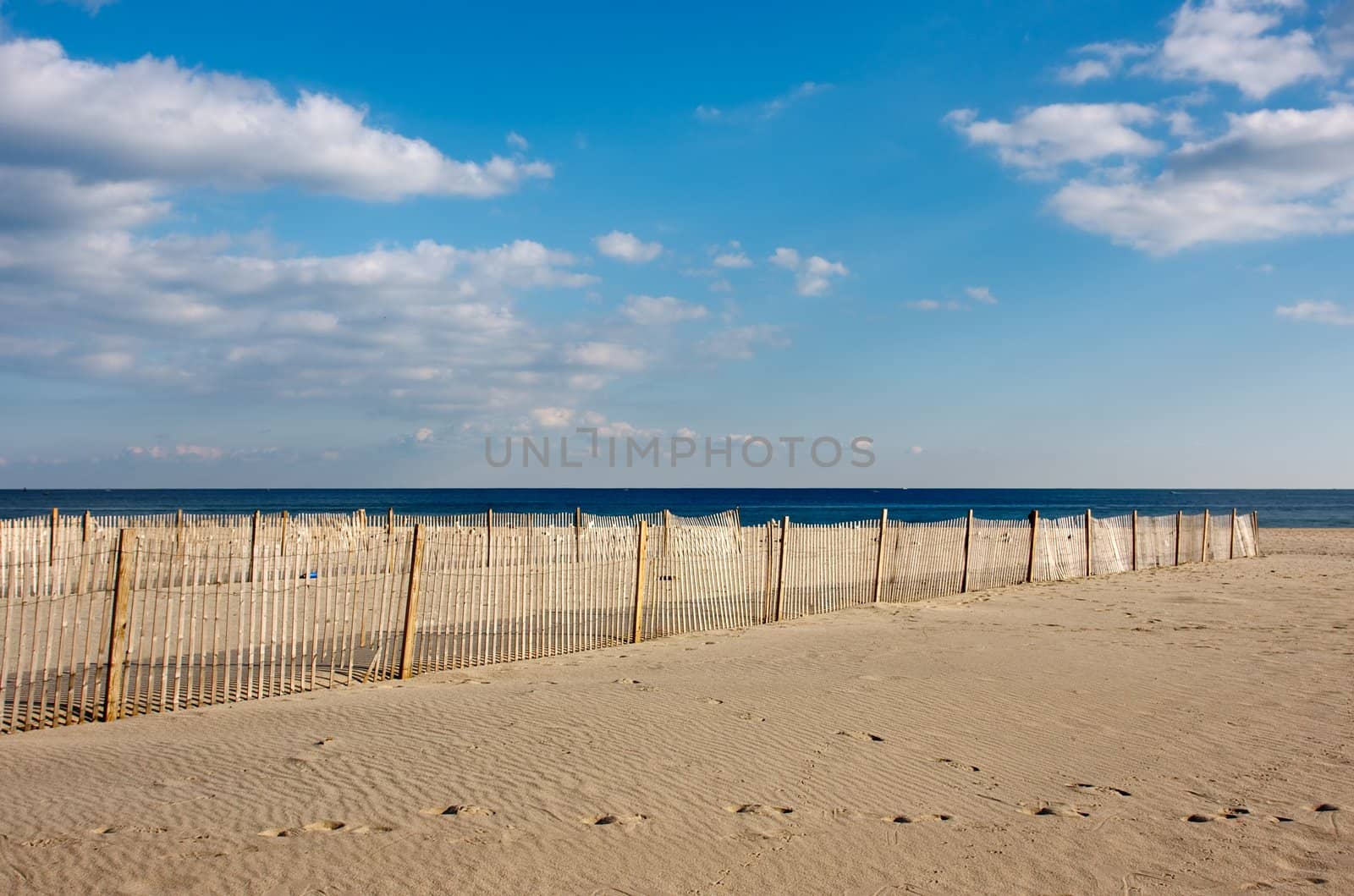 A wooden fence on the beach, The fence is on the sand in the foreground with the ocean and sky above.