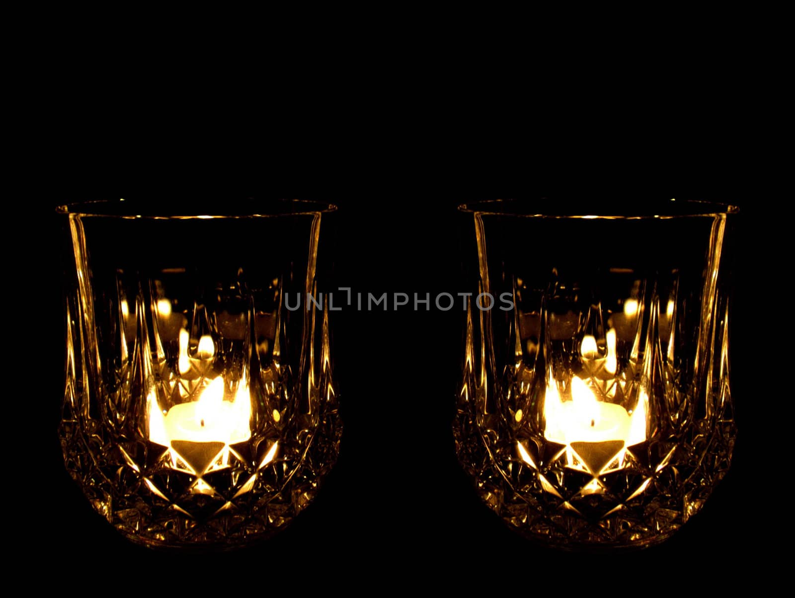 A lead crystal whisky glass illuminated by a tealight candle, against a black background