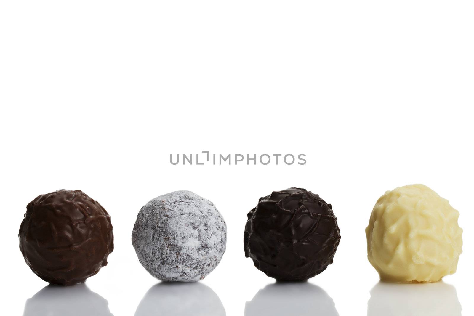 four different truffle pralines in a row on white background