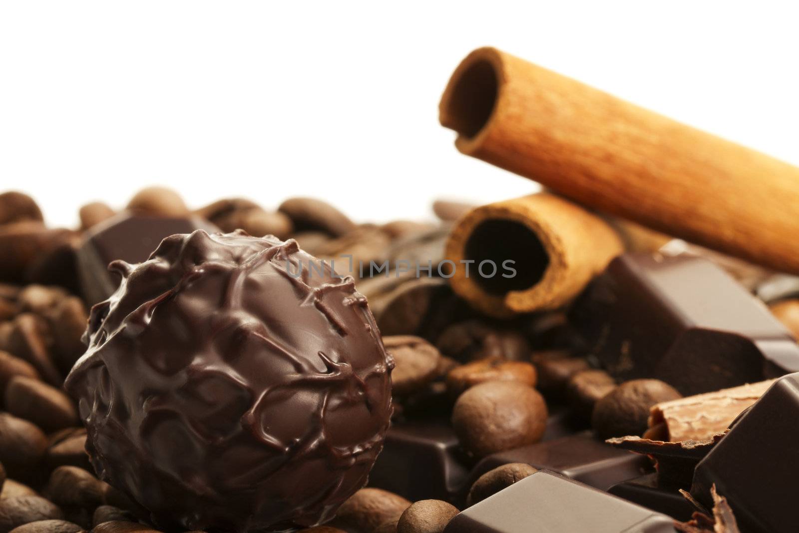 plain truffle praline in front of cinnamon sticks and coffee beans on a plain chocolate bar