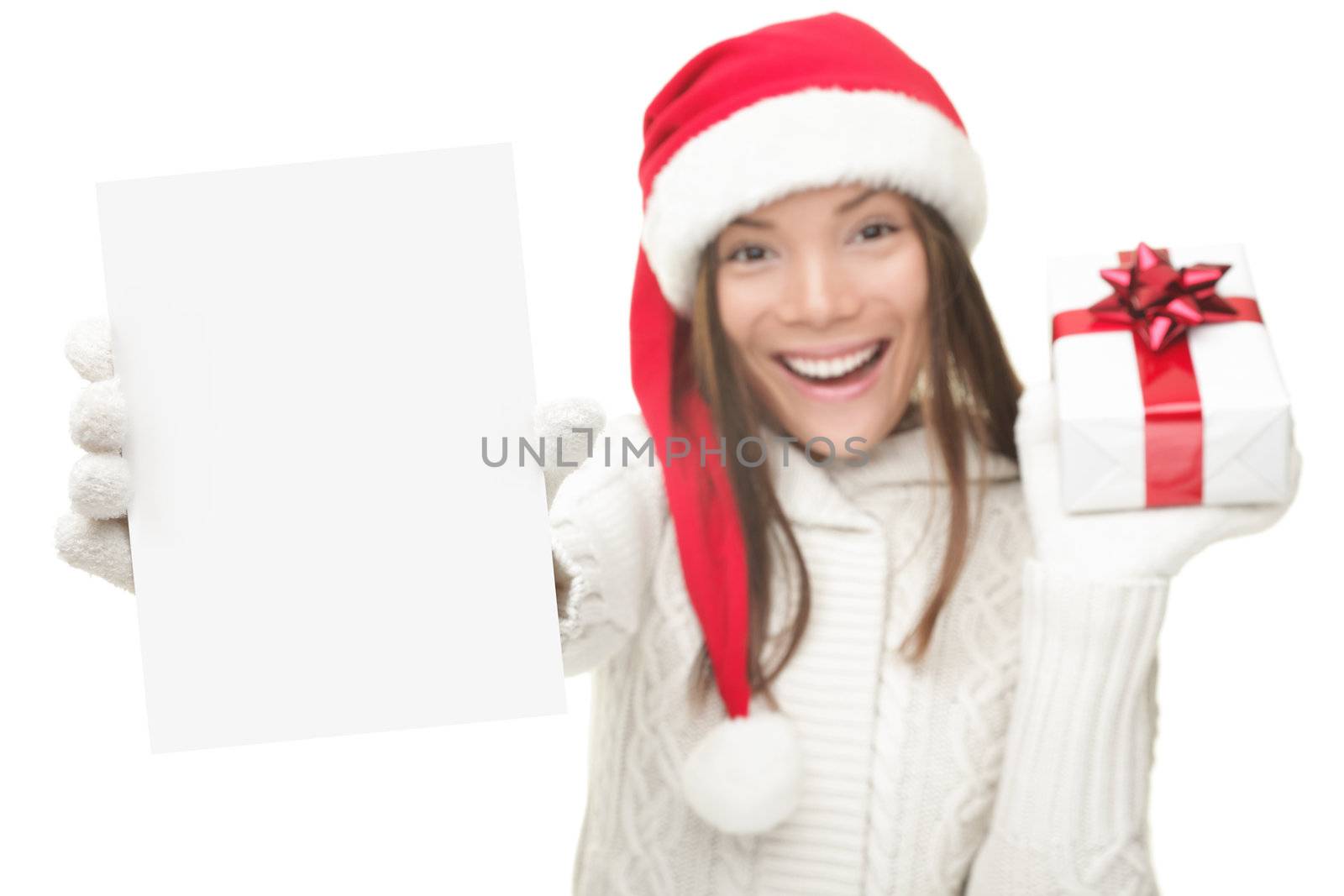 Christmas woman showing blank sign with empty copy space. Beautiful young smiling woman in Santa hat holding white paper card sign. Caucasian / Asian model isolated on white background. Shallow DOF, focus on card.