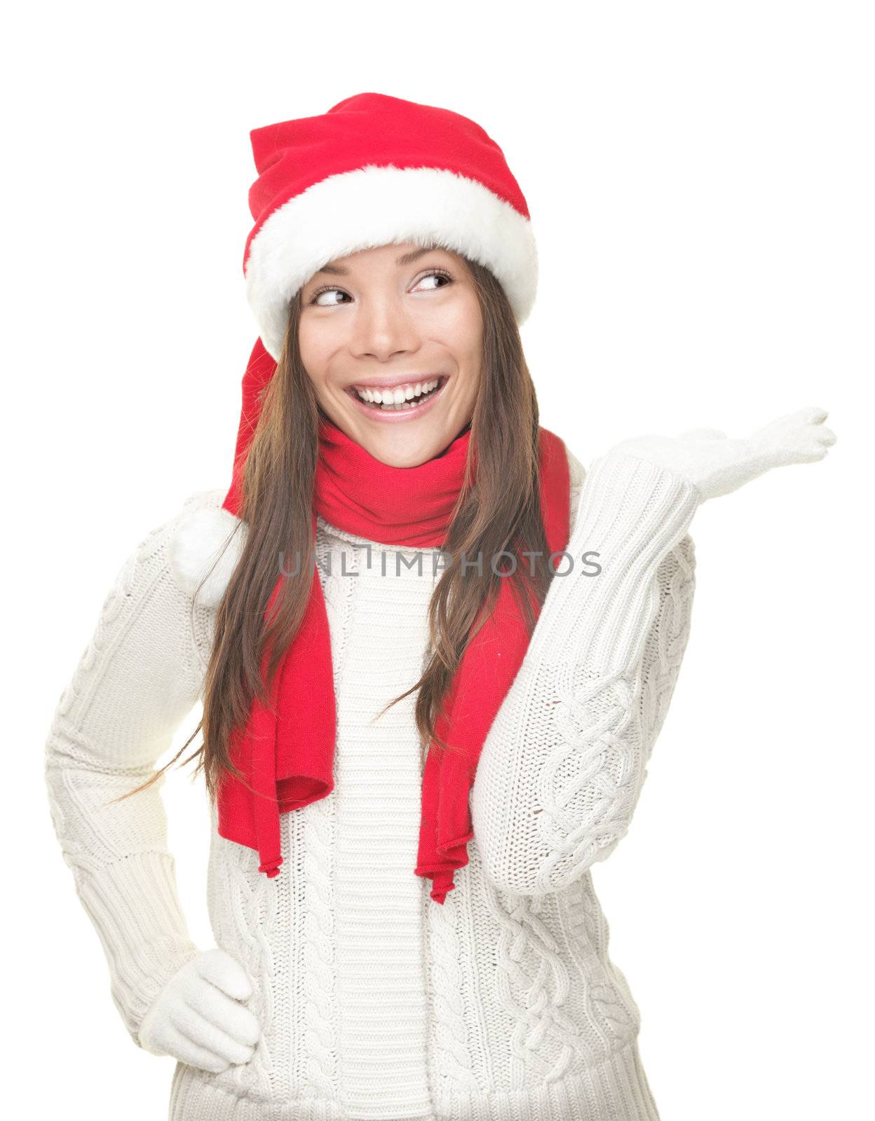 Christmas woman showing copy space looking sideways with open hand palm with room for product or text. Santa girl smiling wearing sweater, scarf and red Santa hat. Beautiful happy Caucasian / Asian woman isolated on white background.