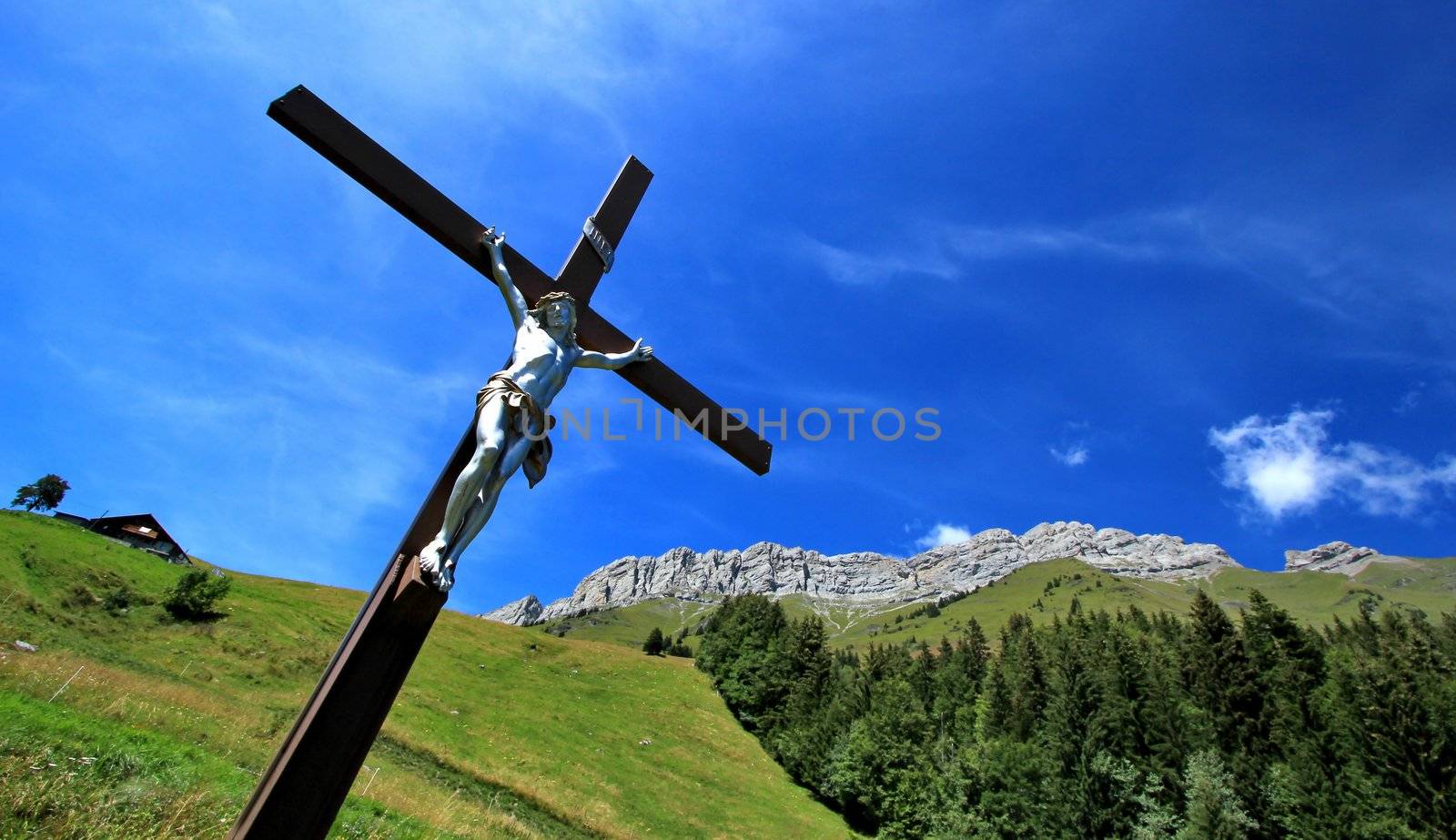 White sculpture of Jesus on a wood cross in the green mountain by summer