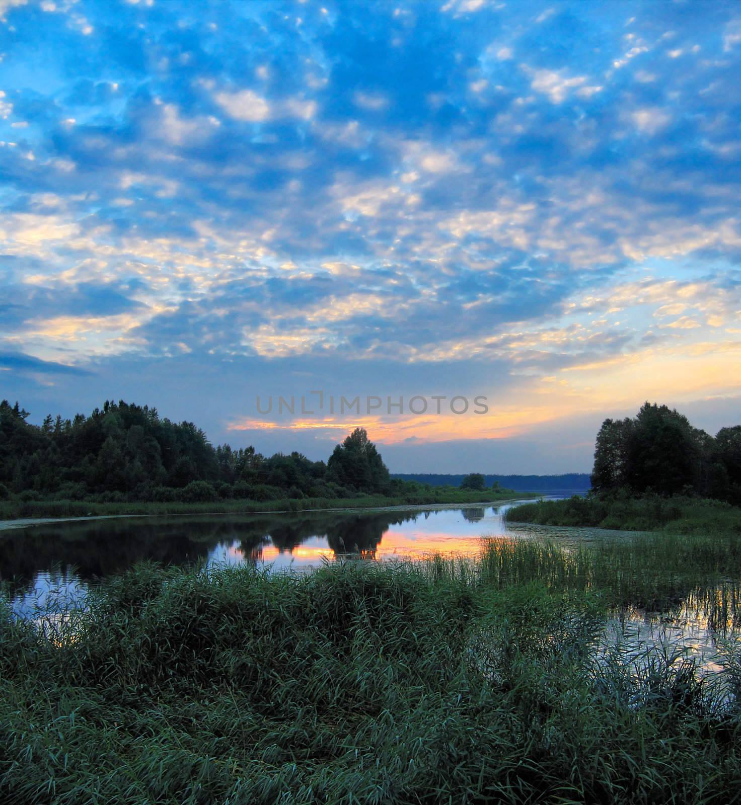 over sunset clouds illuminate blue sky over evening lake