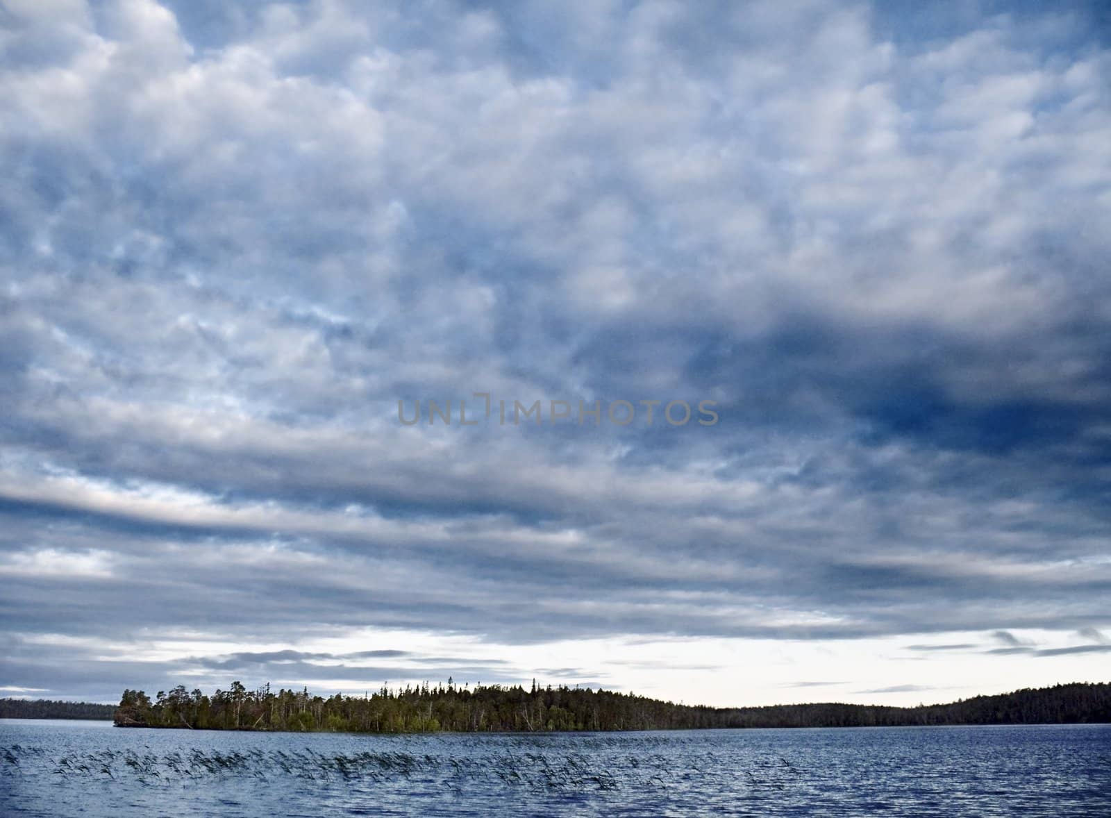 The evening sun through clouds shines cold waters of northern lake