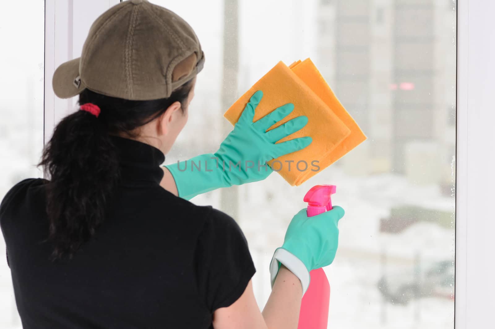 The woman in a cap and green gloves washes a window