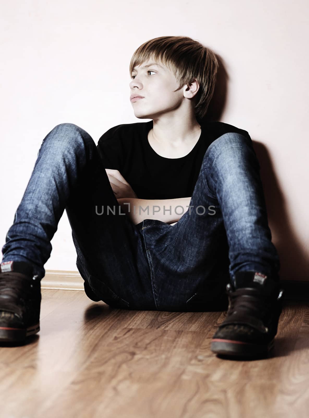 The teenager in a black vest sits about a wall
