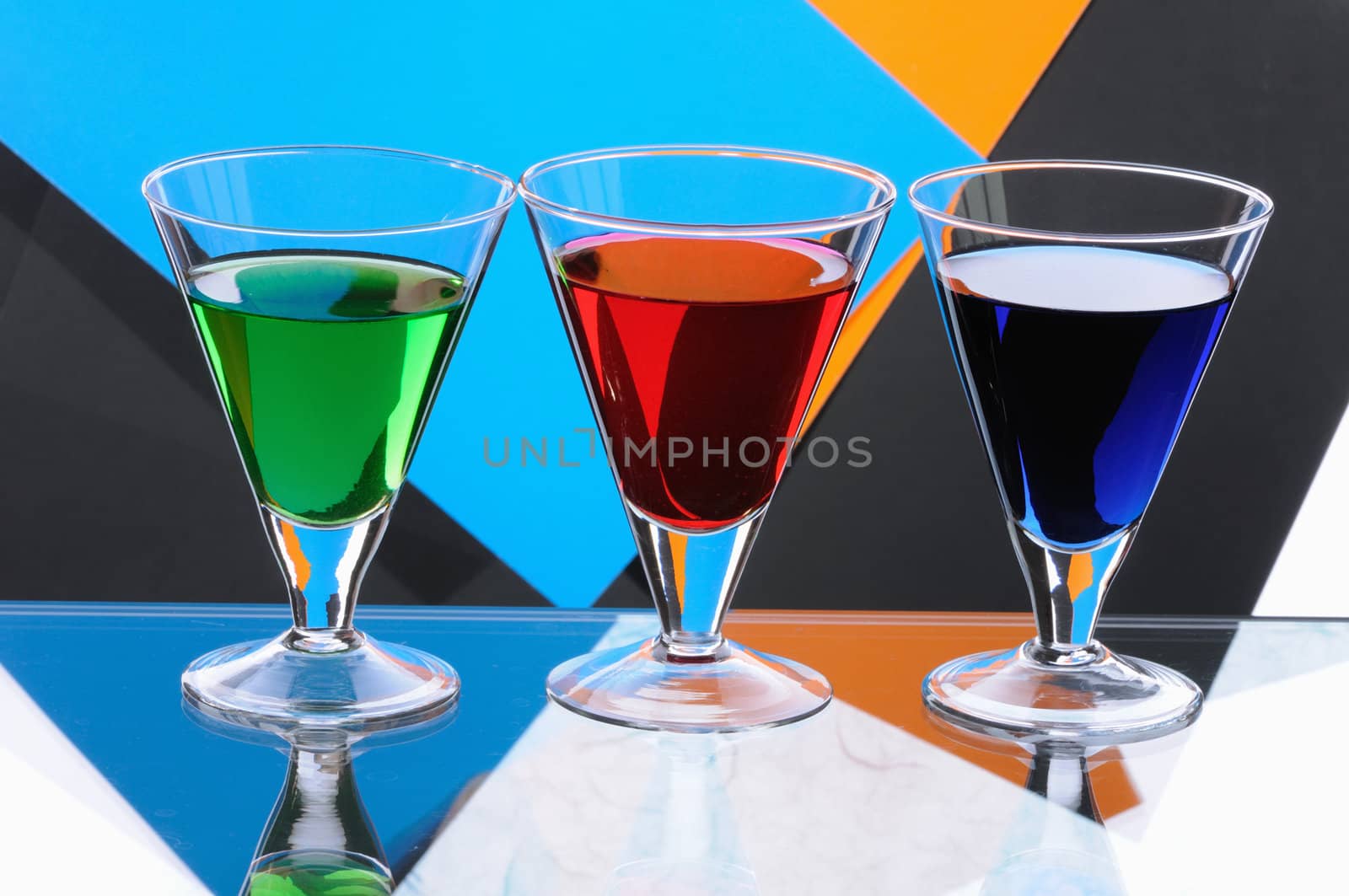 Three transparent glasses with multi-coloured drinks