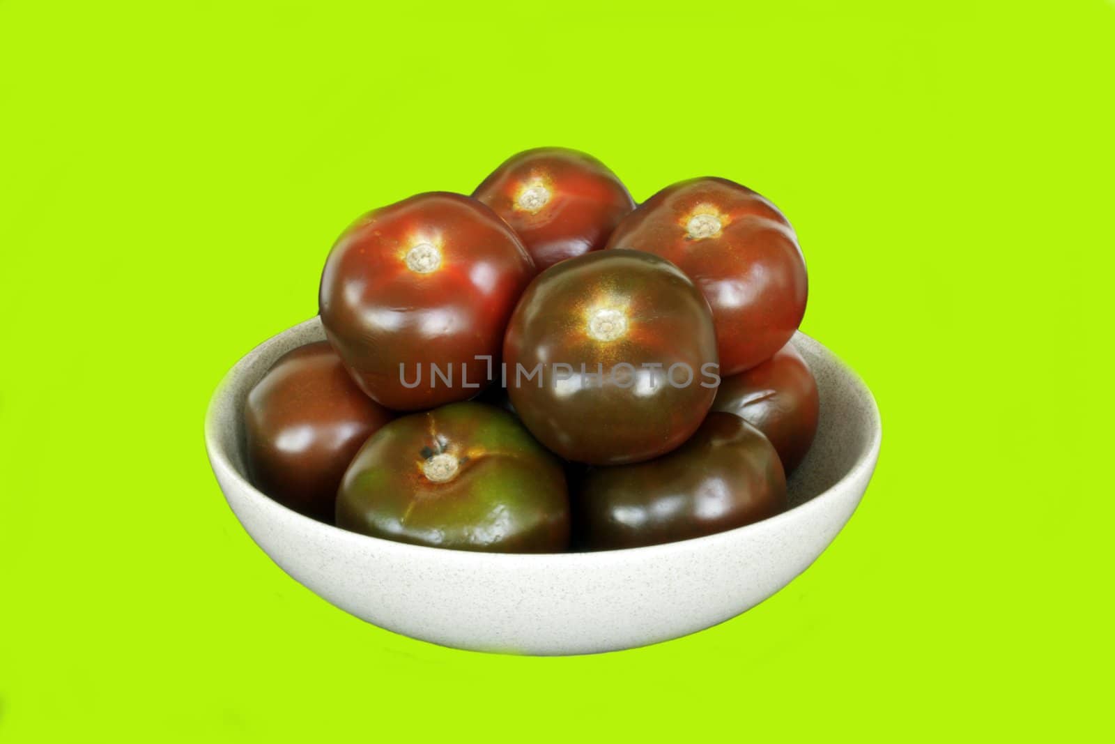 Red dark salad tomatoes on ceramic dish in isolated over green