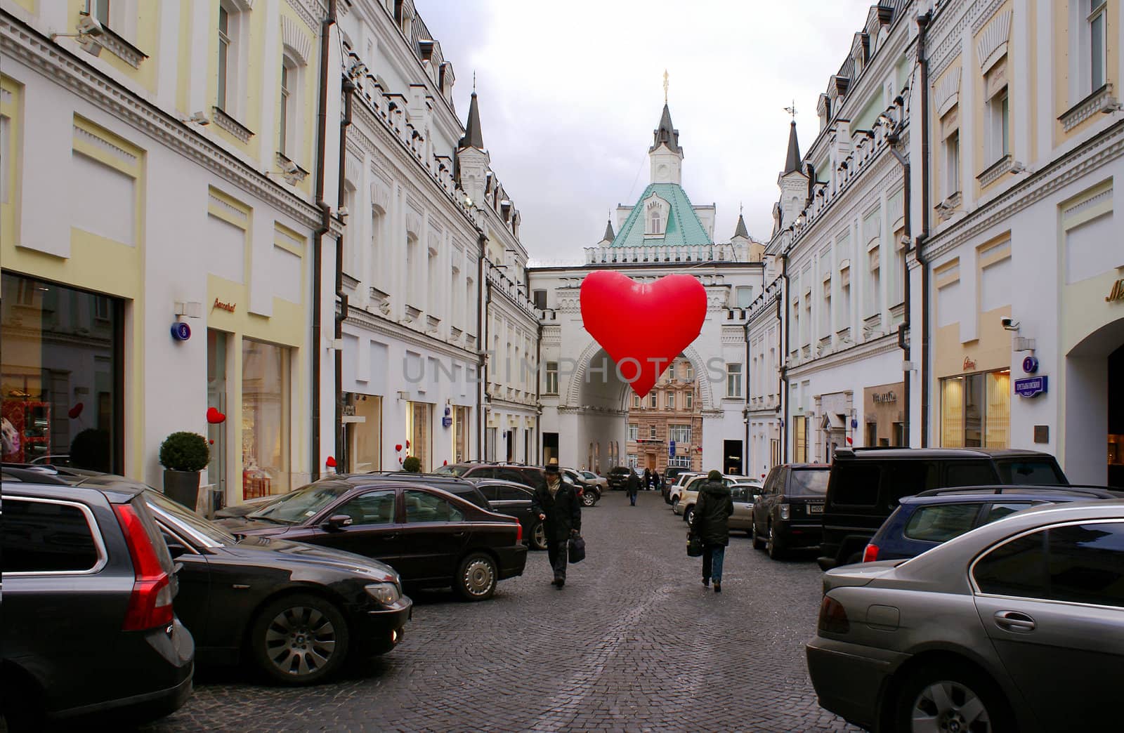 Big red heart ballon is hanging over old street.