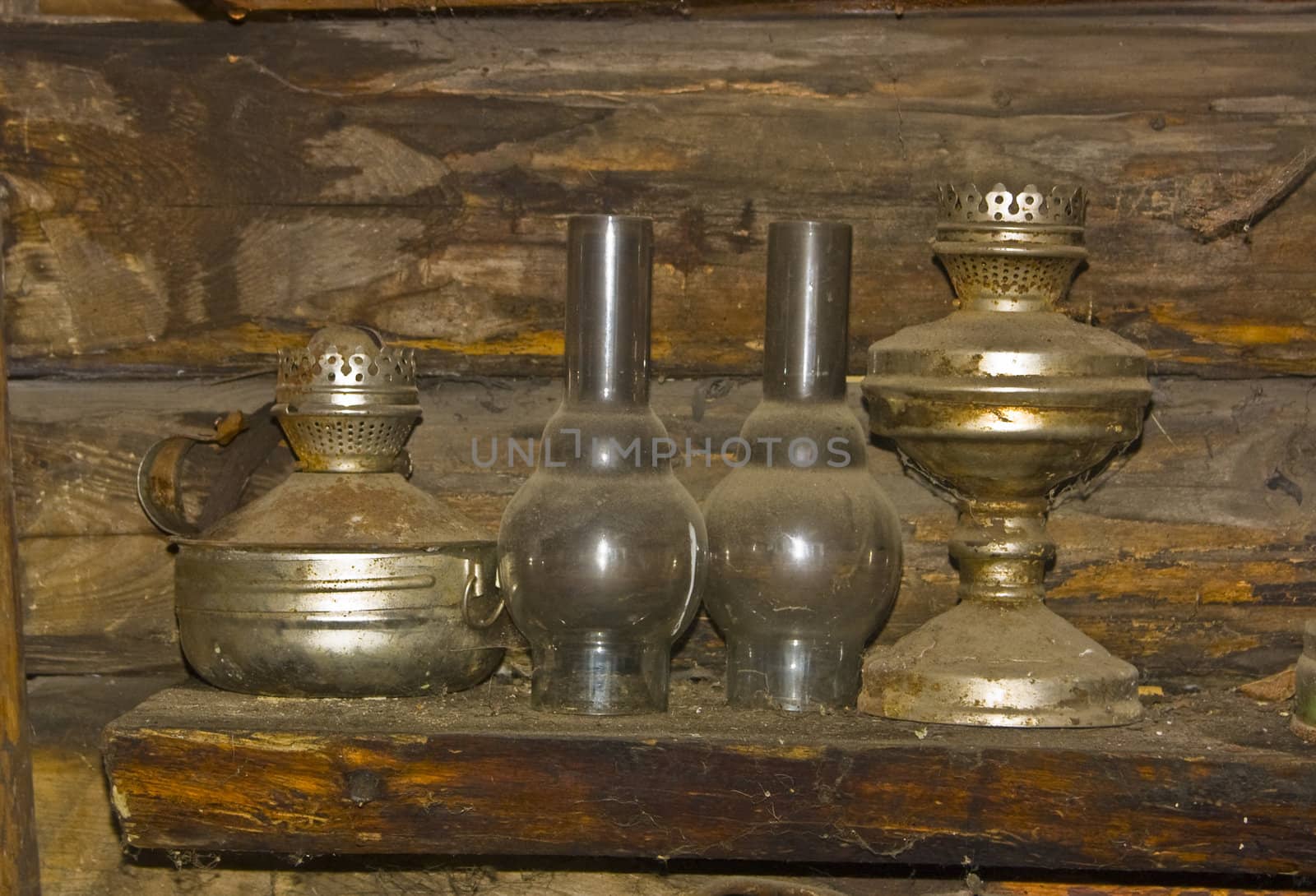 Image of two old kerosene lamps, standings in a dust on a wooden shelf