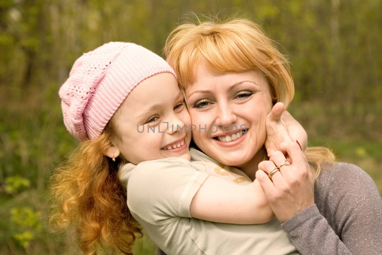 The beautiful little girl in a pink cap embraces mum with light hair
