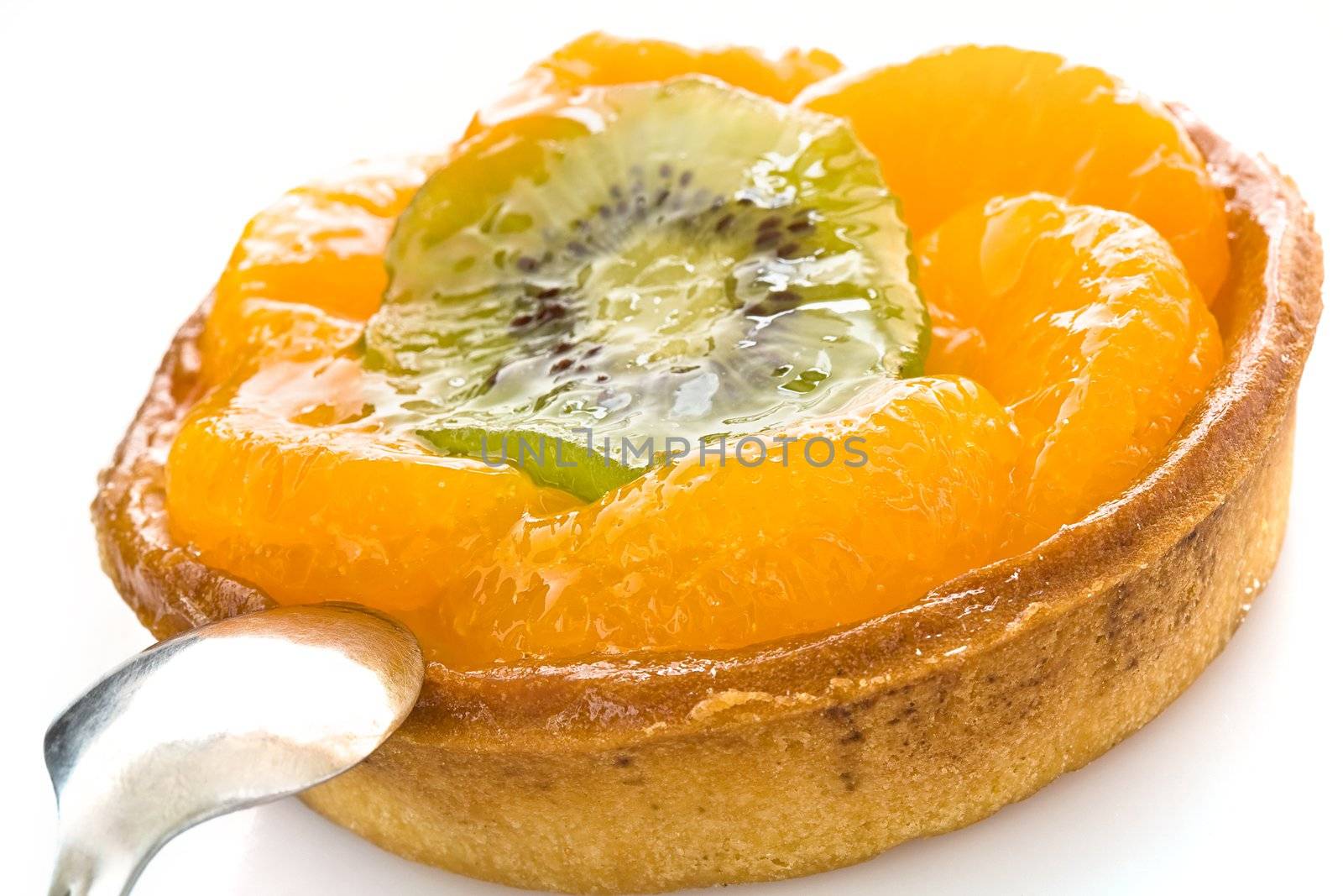 Round cake with segments of a tangerine and a circle of kiwi close up on a white background with a spoon
