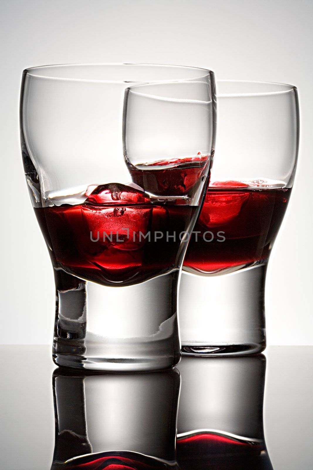 Elegant still-life from two glasses half filled with a red translucent liquid with ice 