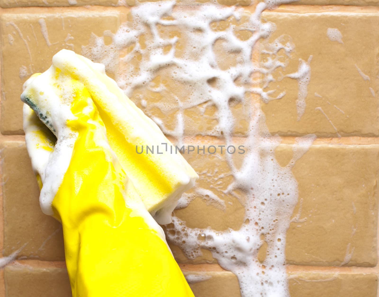 hand in yellow rubber glove holding soapy cleaning sponge 