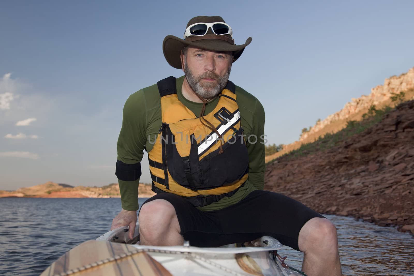 mature male boarding his canoe on a mountain lake with red sandstone cliffs (Horsetooth Reservoir near Fort Collins, Colorado)