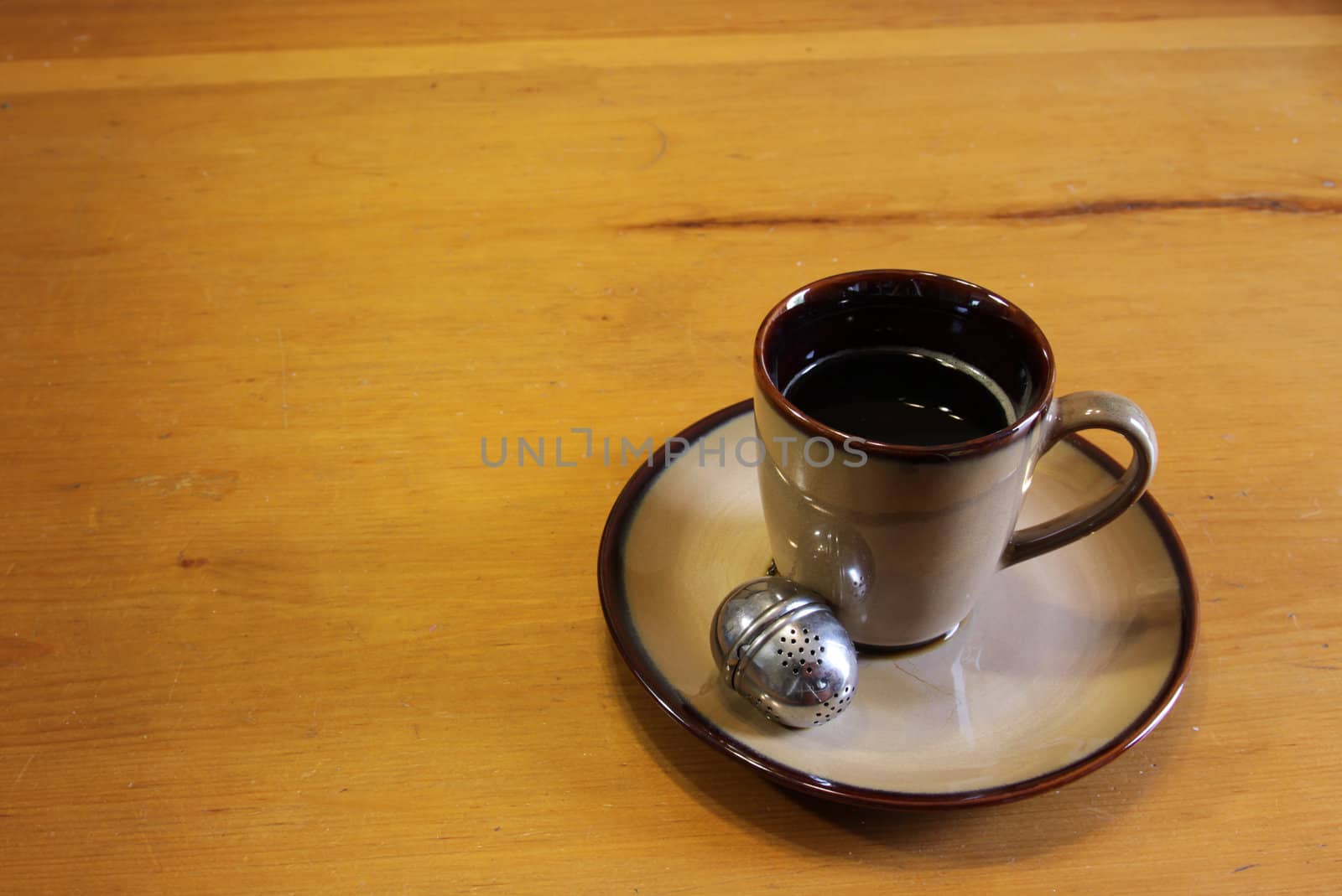 A tea strainer sitting next to a mug of hot freshly brewed tea.
