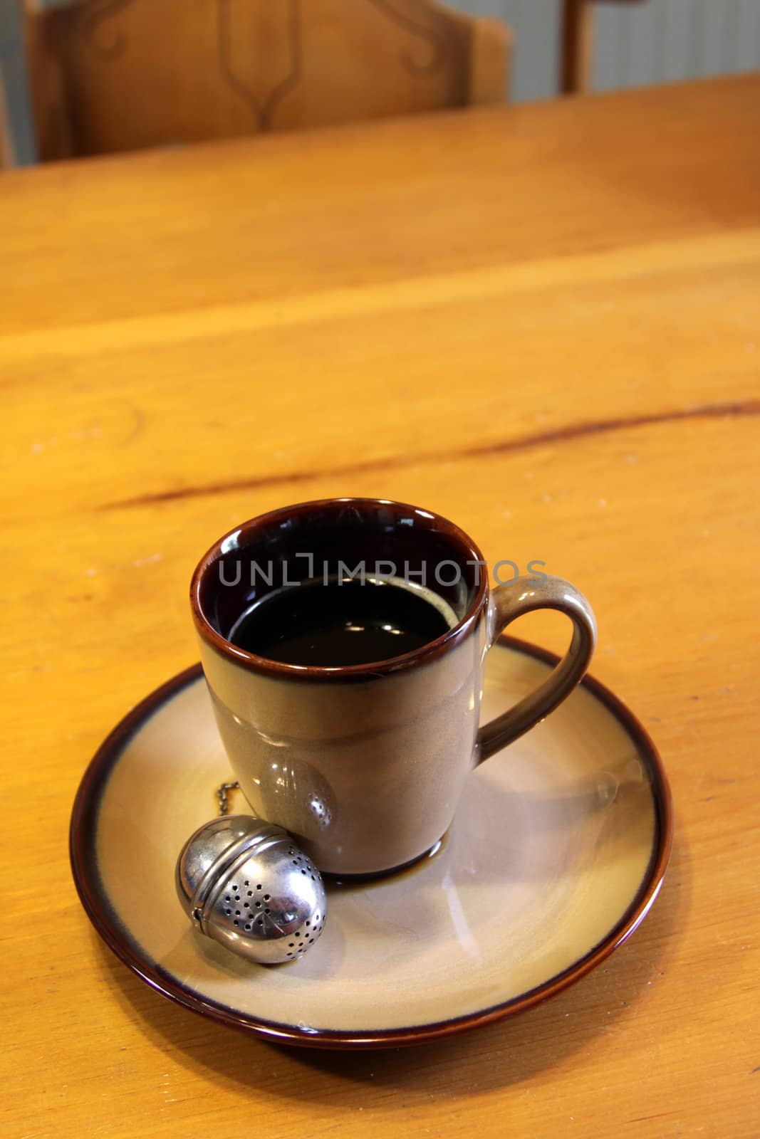 A tea strainer sitting next to a mug of hot freshly brewed tea.
