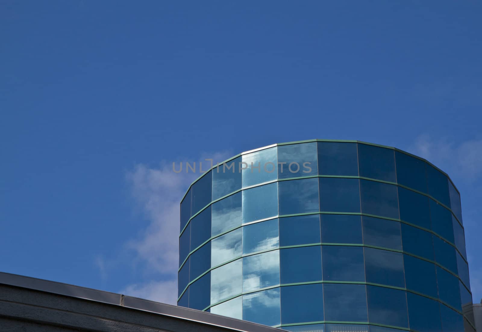 Angled reflective windowed Cylinder Building reflecting blue sky and clouds