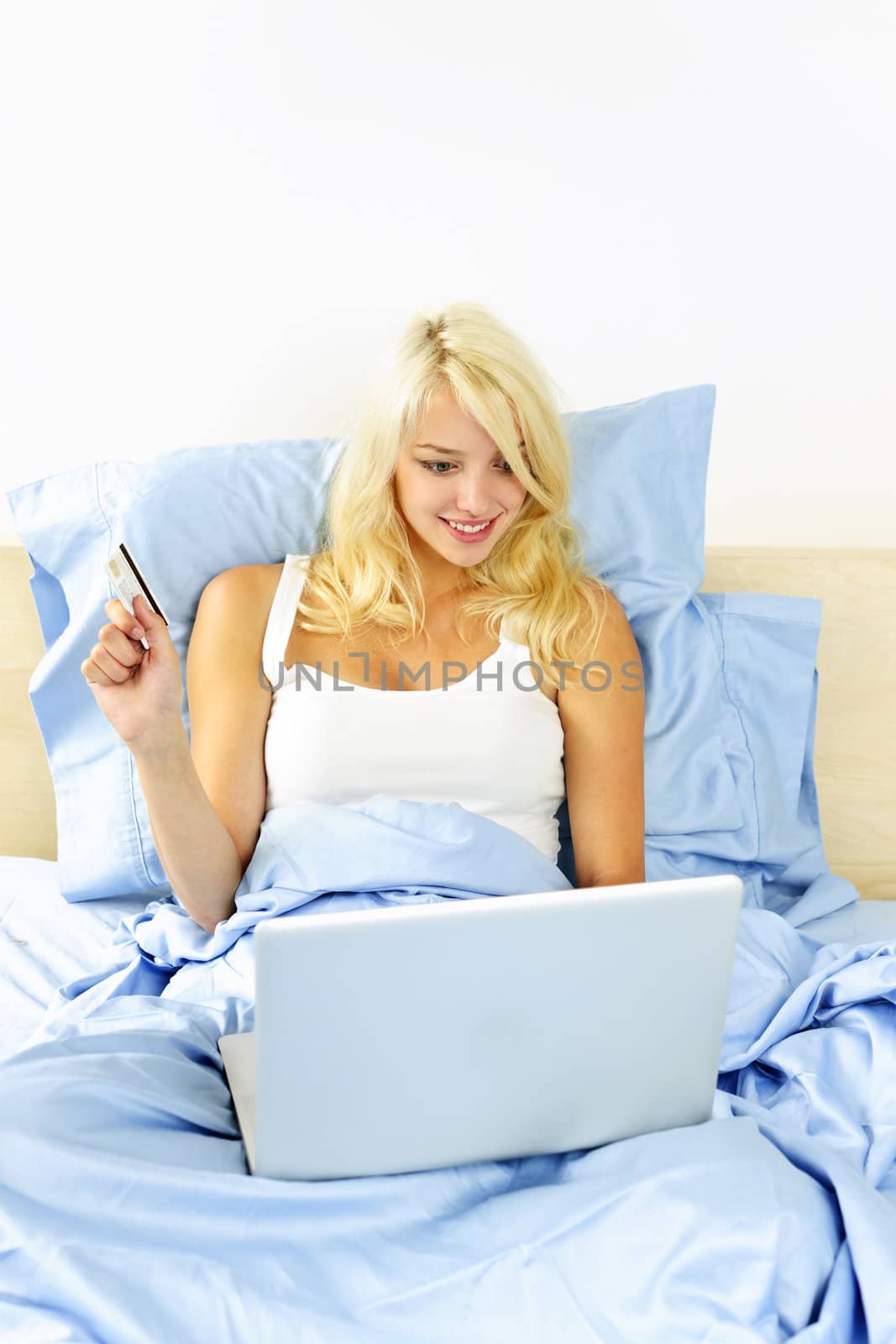 Woman shopping online in bed with computer by elenathewise