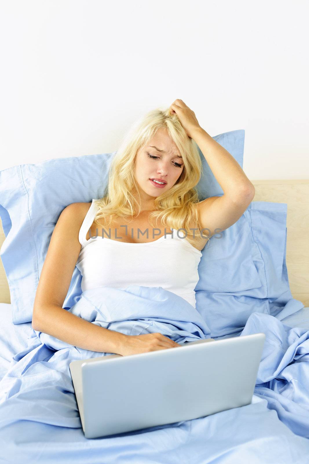 Worried blonde woman using laptop computer sitting in bed