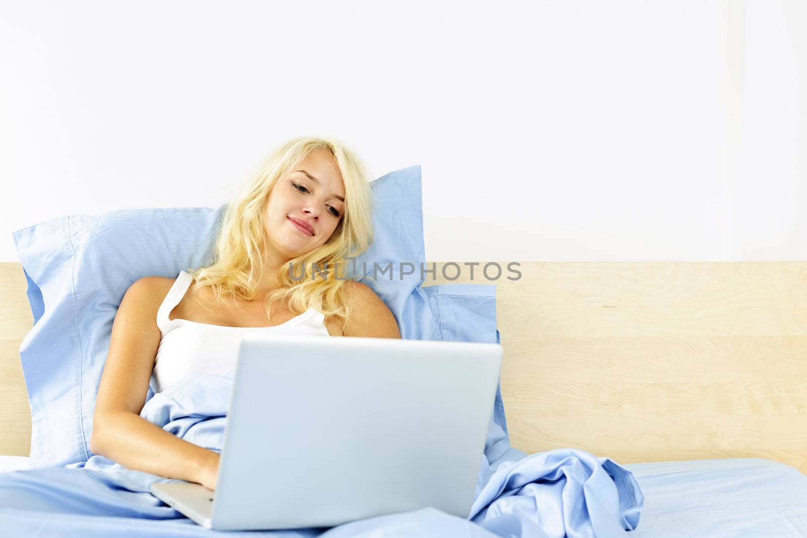 Woman sitting in bed with computer by elenathewise