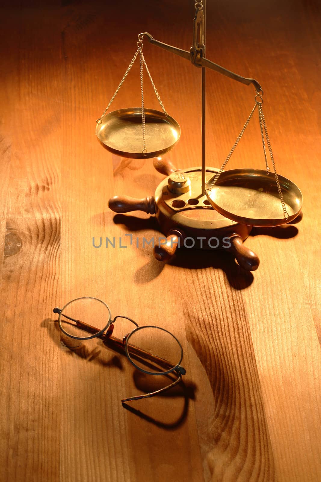 Ancient brass weight scale standing near old spectacles on nice wooden background