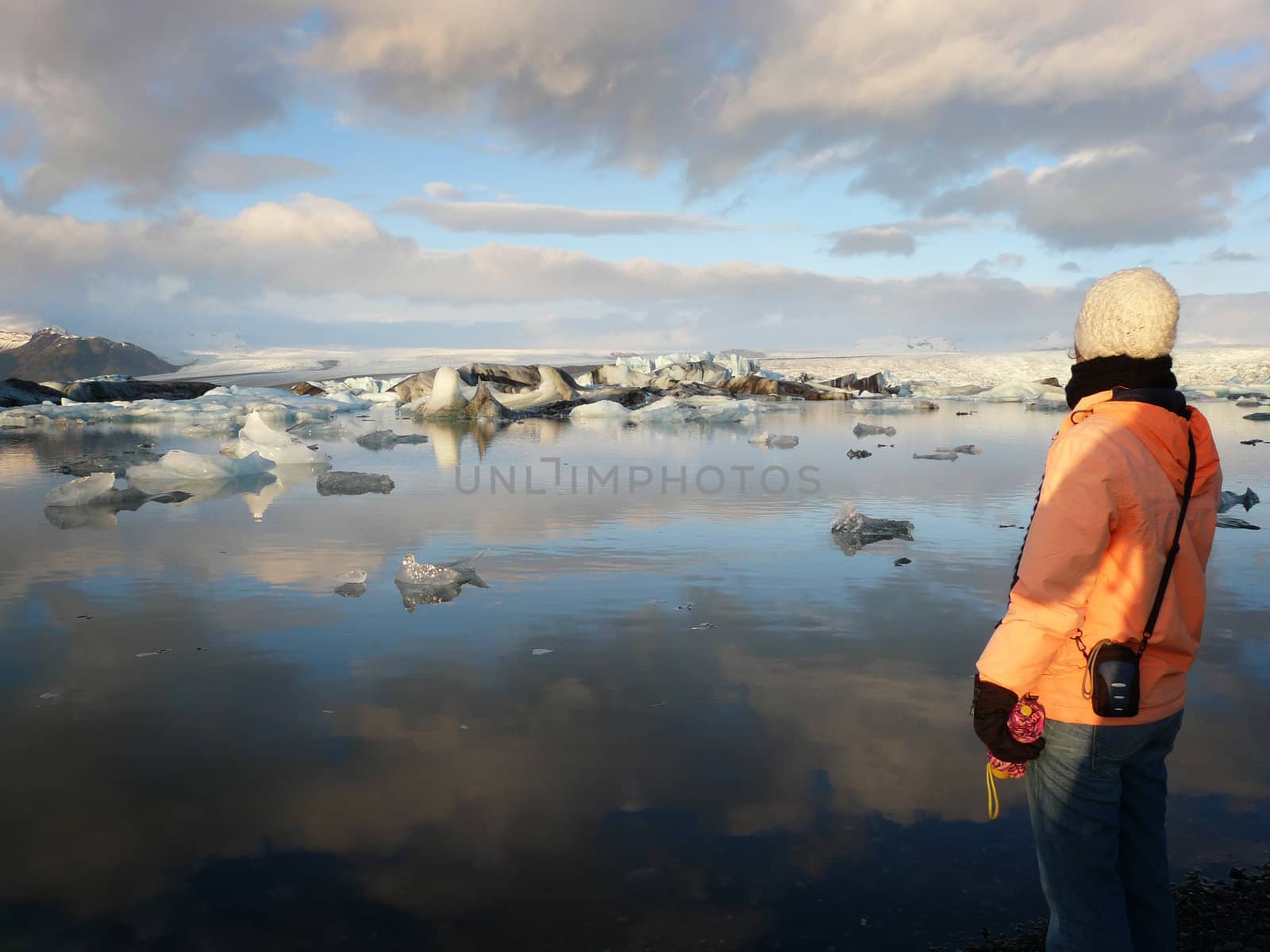 Young woman admiring Jokulsarlon, a lake in Iceland, where icebergs collapsing from Vatnajokull glacier are floating around.