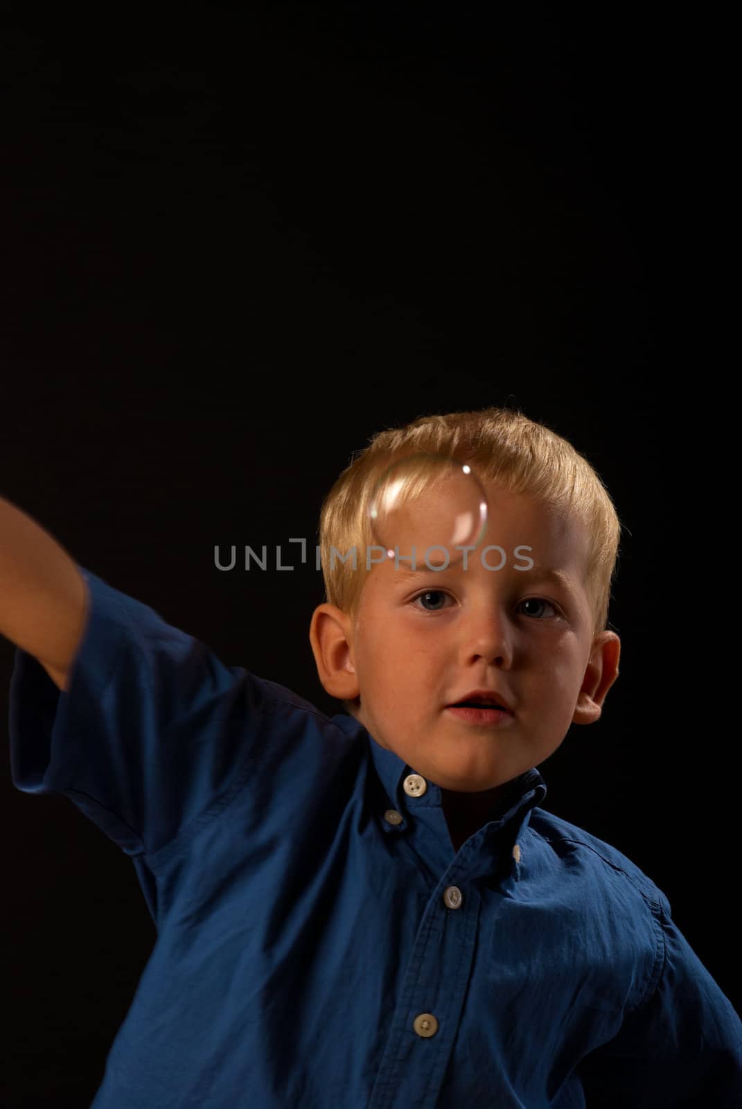 Blond boy concentrated trying to catch a soap bubble