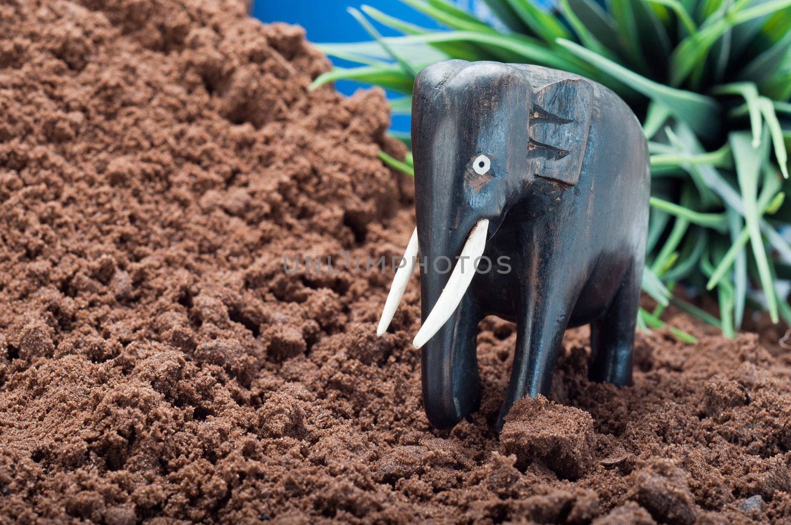 Wooden African elephant carving on sand with green plant and blue sky in the background