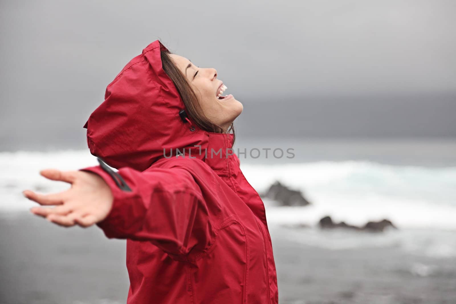 Rain. Woman enjoying a grey rainy fall day on the beach. Young smiling woman in red raincoat.