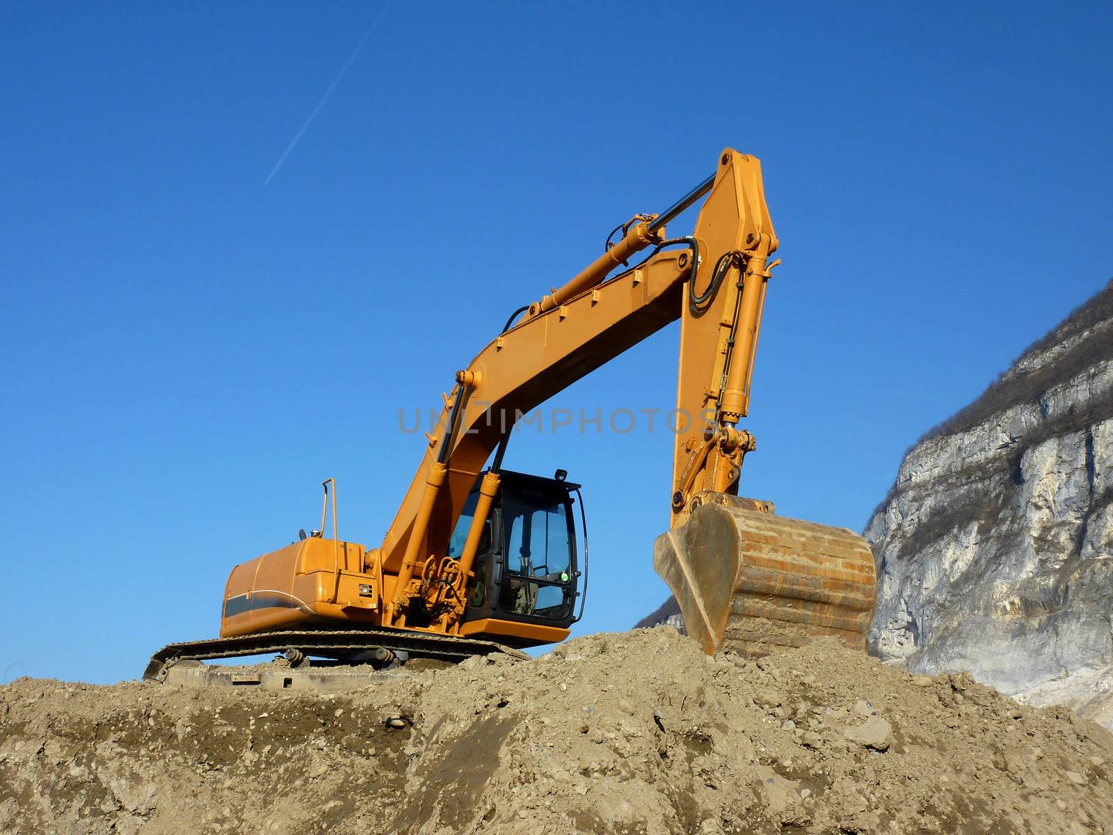 Big orange excavator standing on ground next to a mountain