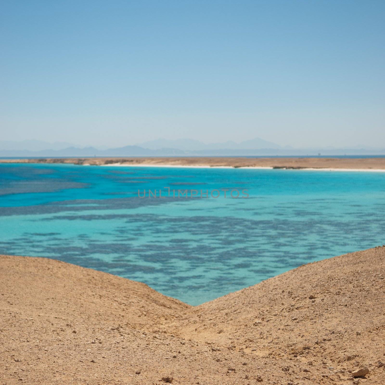 Turquoise waters and gentle waves of a golden sand beach with deep blue sky.