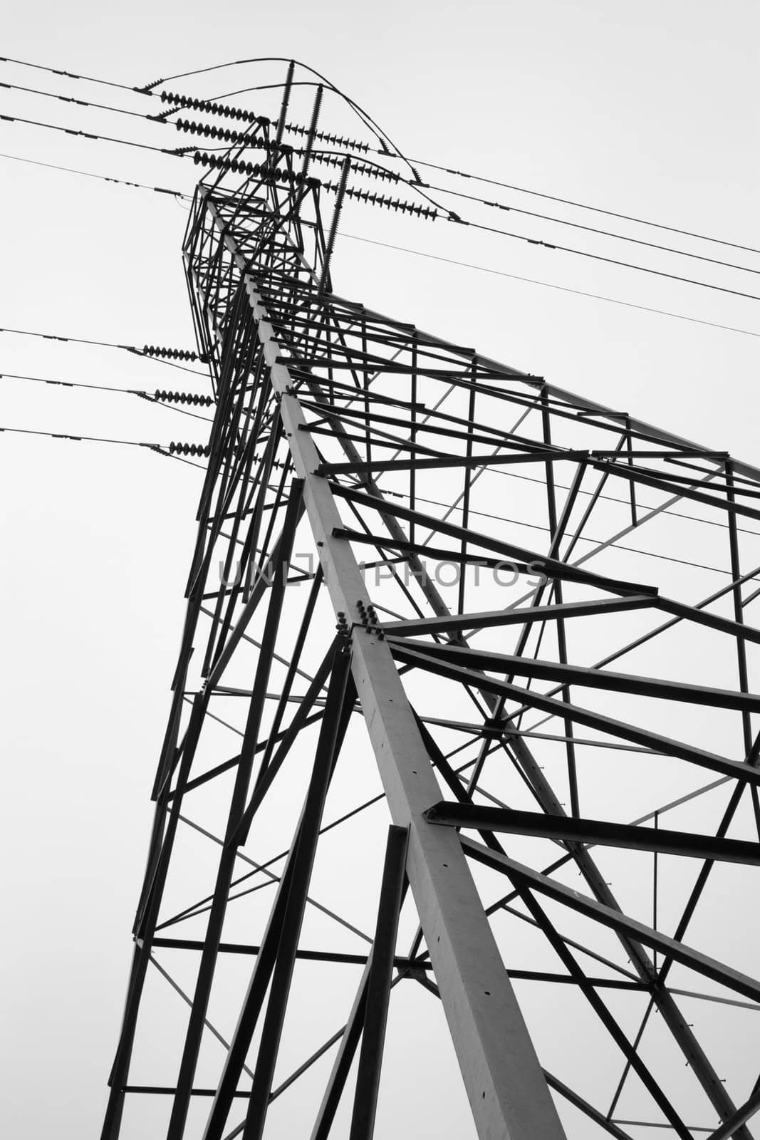 Side view of electric power tower looking from the base to the top against cloudy sky
