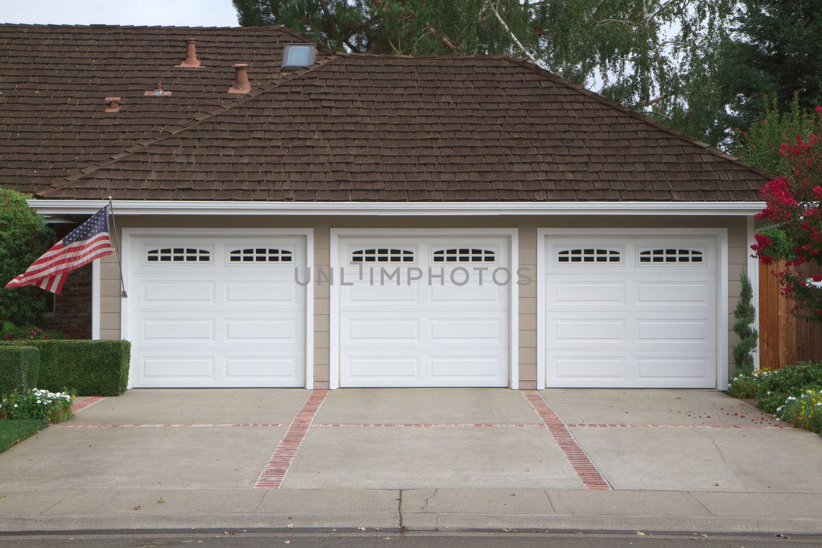 Beige three ar garage with white doors and brick and red brick driveway