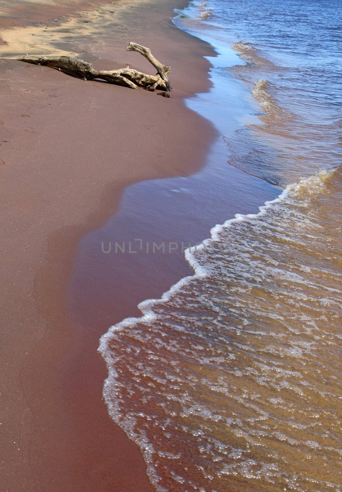 Tranquil waves running over red sand coast.