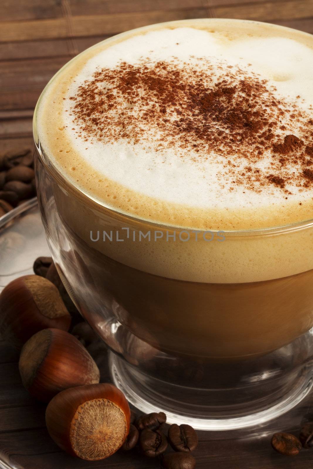 cappuccino with chocolate powder on milk froth and hazelnuts on wooden background