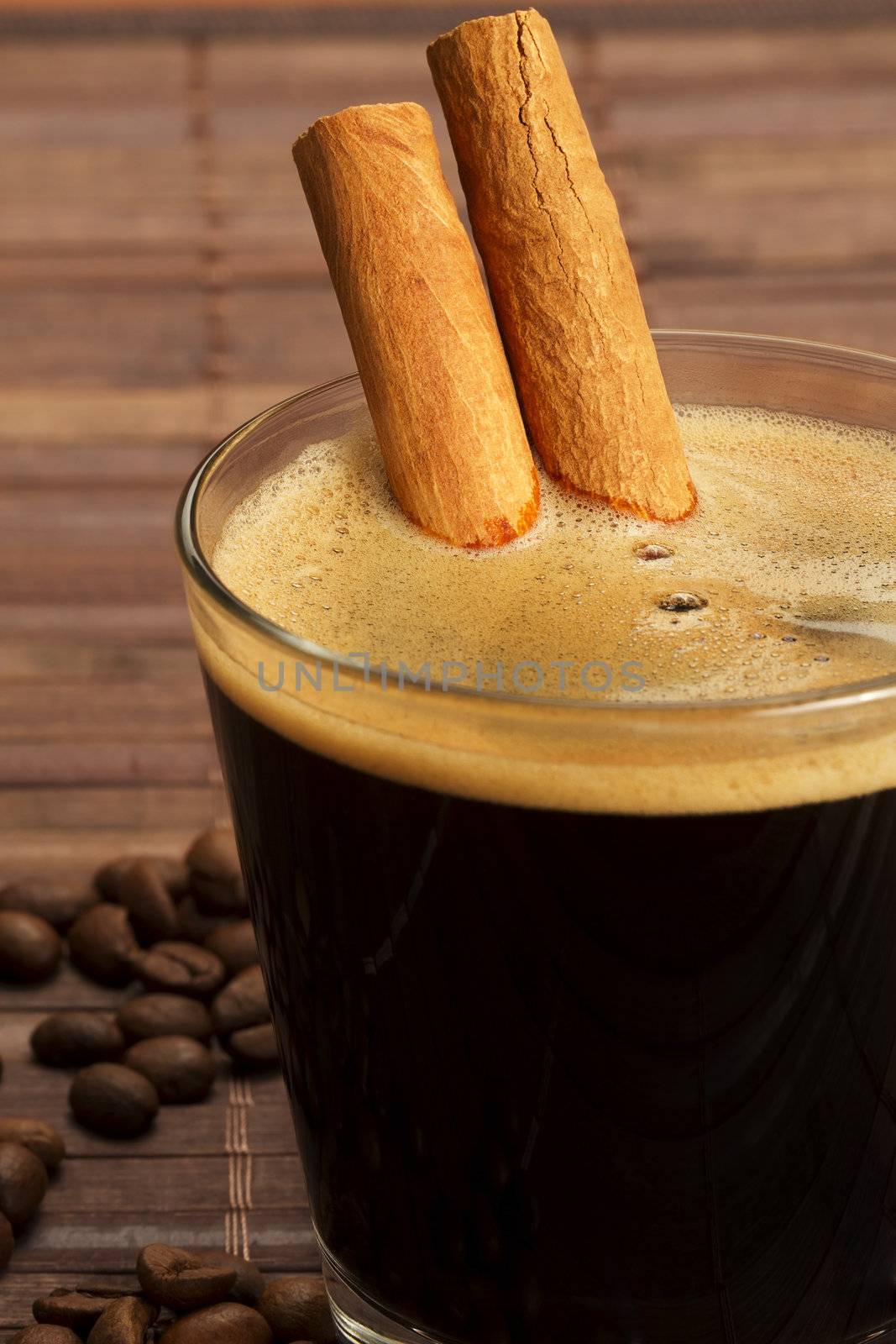 cinnamon sticks inside espresso in a short glass coffee beans aside on wooden background