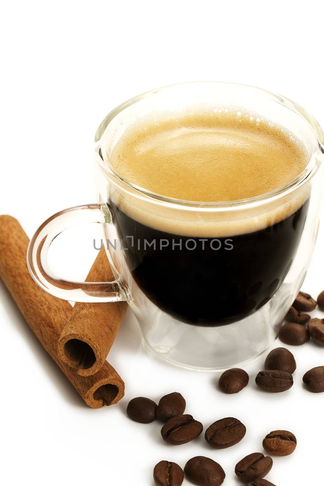 espresso in a glass cup with cinnamon sticks and coffee beans on white background
