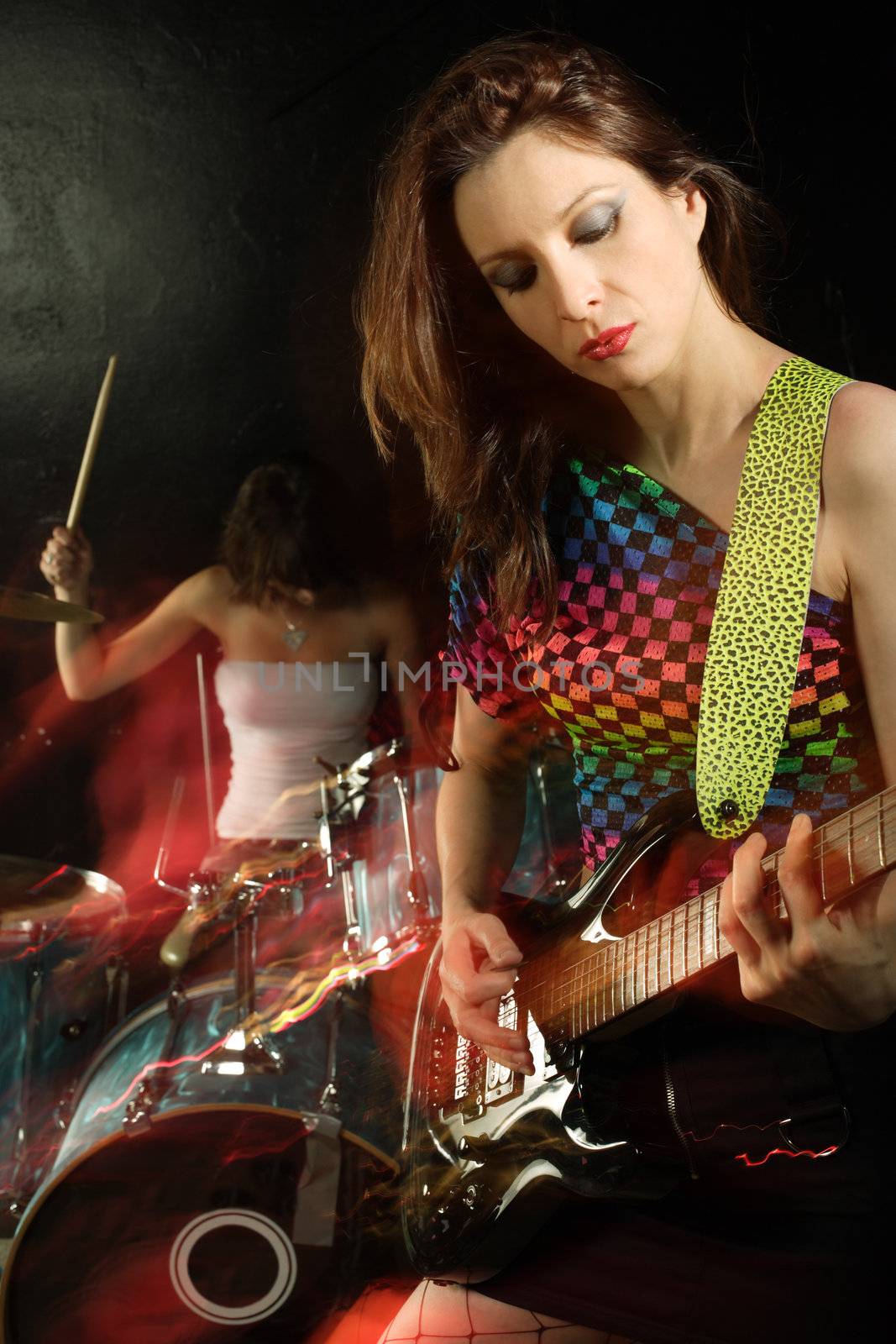 Photo of a female guitarist playing on a stage. Shot with strobes and slow shutter speed to create lighting atmosphere and blur effects. Slight motion blur on performer.